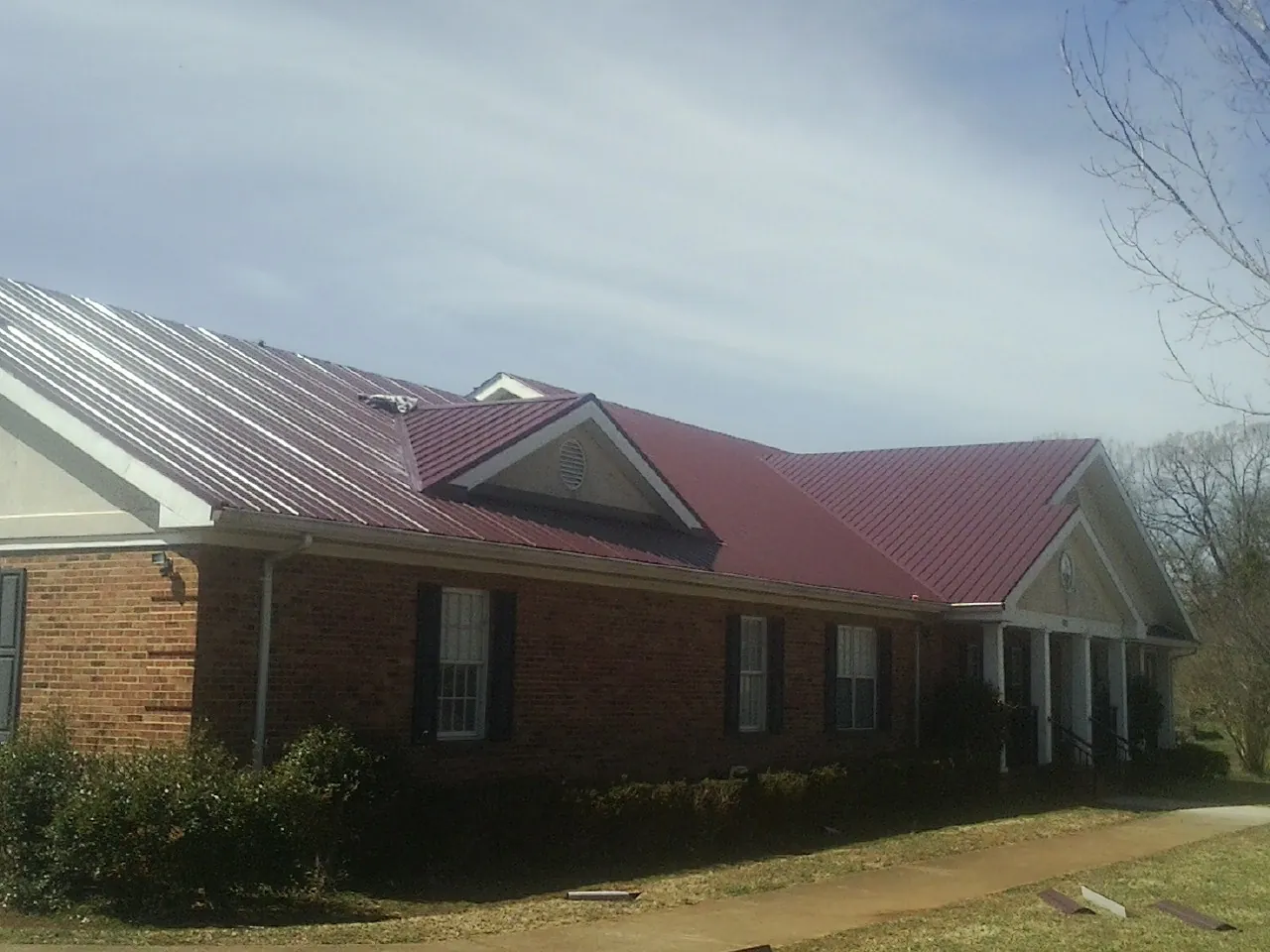 Red metal roof with gabled entries on a long brick building, from a Hail Damage Roof Repair job in Dallas